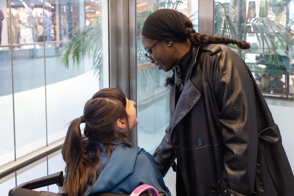 Neurodivergent teenage girl in wheelchair riding an elevator in a shopping mall with her disability support worker.